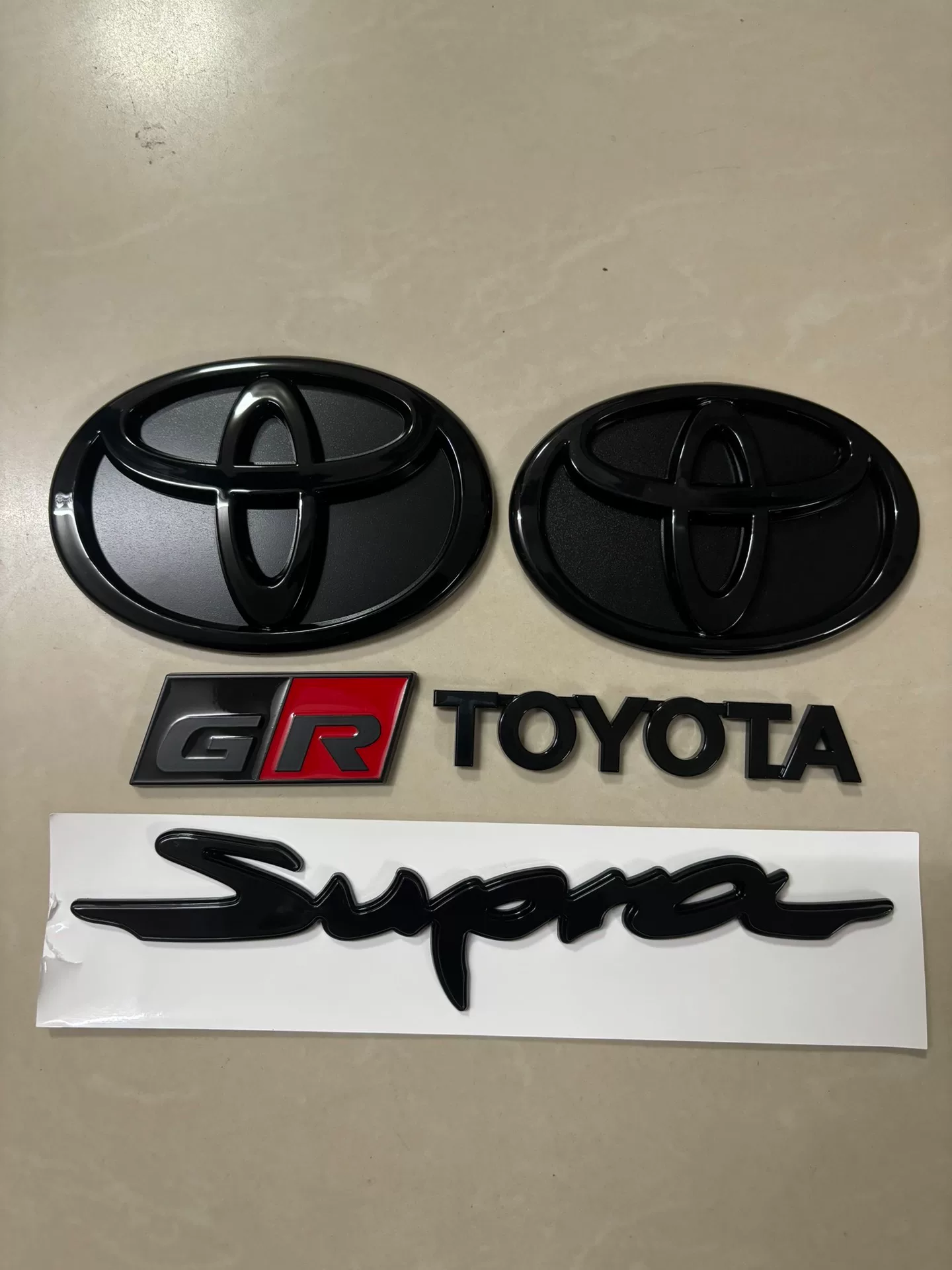 Toyota A90, A91 Used OEM Emblem Badge matte black, red accent A90 Toyota A90, A91 Used OEM Emblem Badge matte black, red accent A90