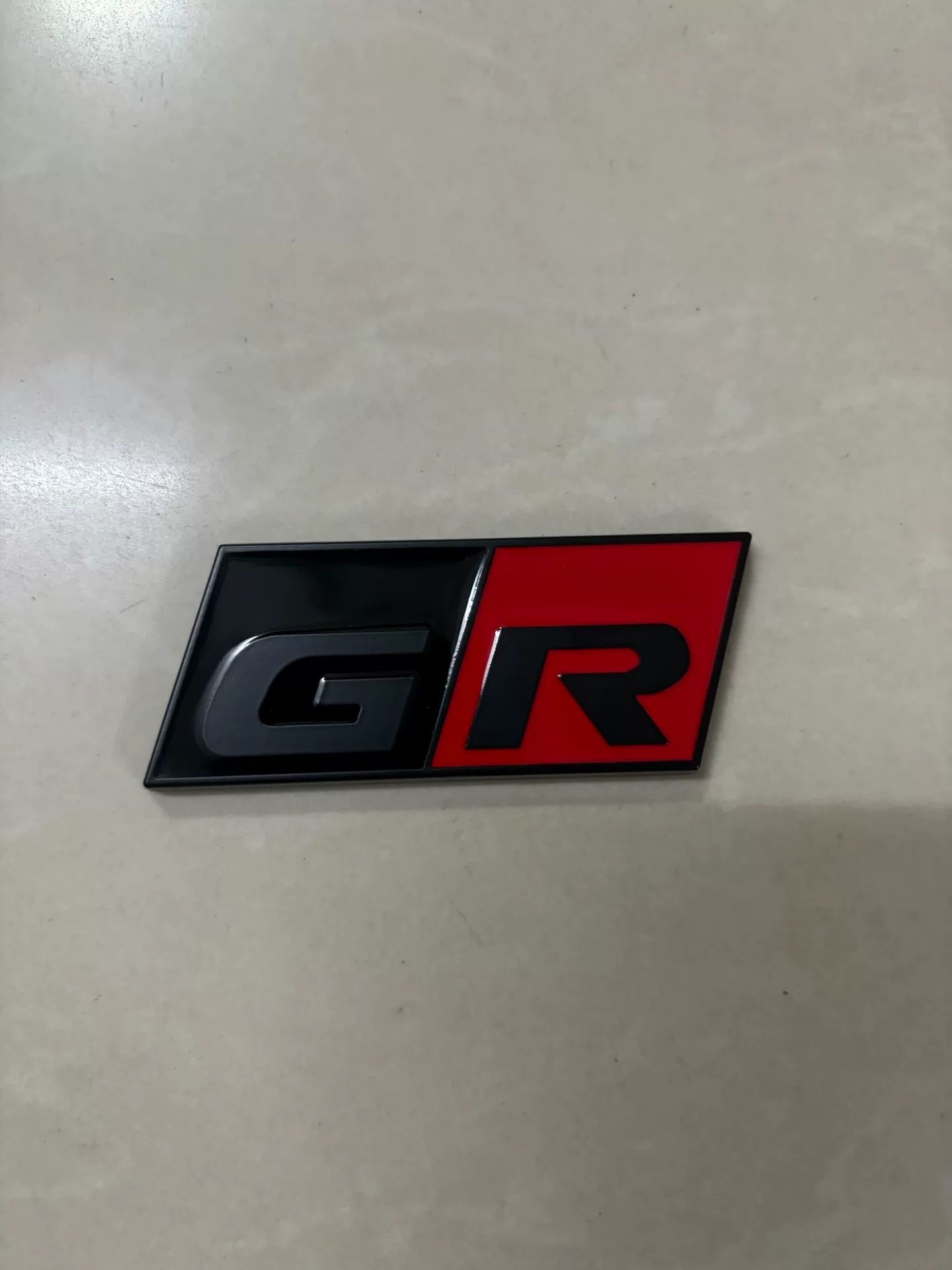 Toyota A90, A91 Used OEM Emblem Badge matte black, red accent A90 Toyota A90, A91 Used OEM Emblem Badge matte black, red accent A90 - detail image 4