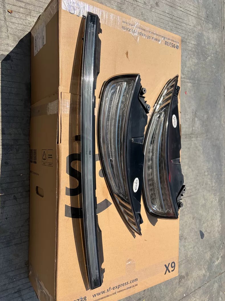 Porsche 911 991.1 clear lens LED rear tail light set: pair of clear lens tail lights and the rear centre reflective trim standing against a shipping box
